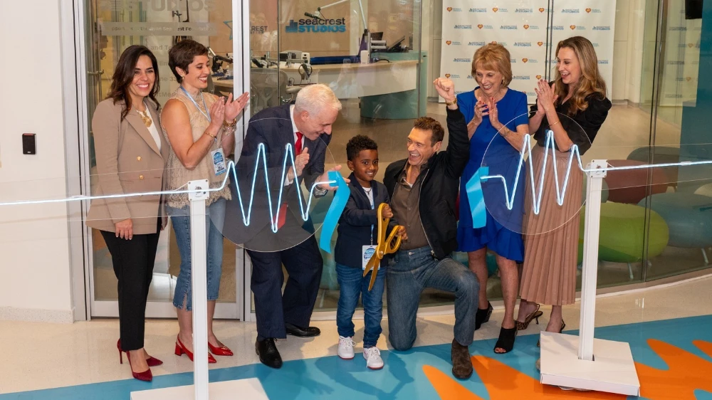 young boy cuts the ribbon for the studio grand opening as the crowd cheers on.