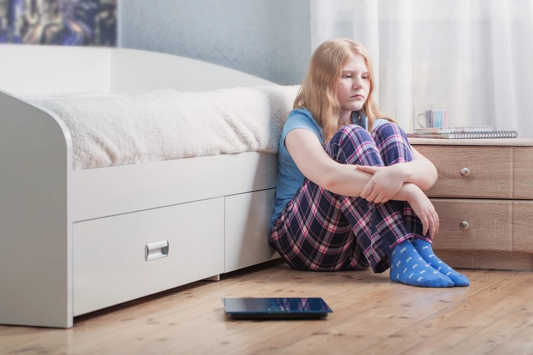 Sad girl sitting next to scale.
