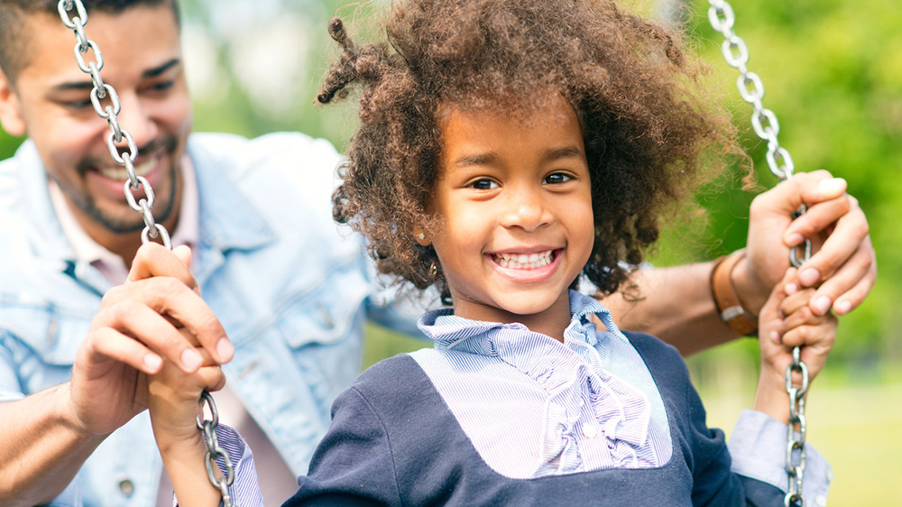 happy african american girl pushed on a swing by her father.