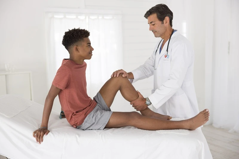 Male doctor examining male teen's knee.