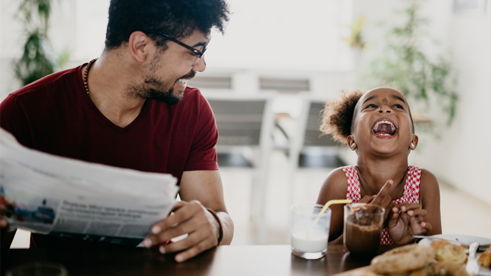 father and daughter laughing as they eat on the kitchen counter.