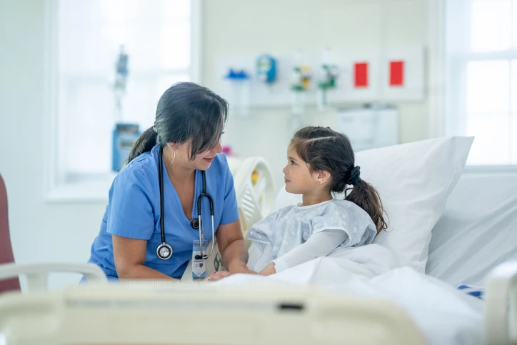 little girl accompanied by nurse at her hospital bediside.