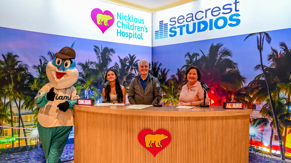 Marlins mascot and hospital staff at the TV announcer desk.