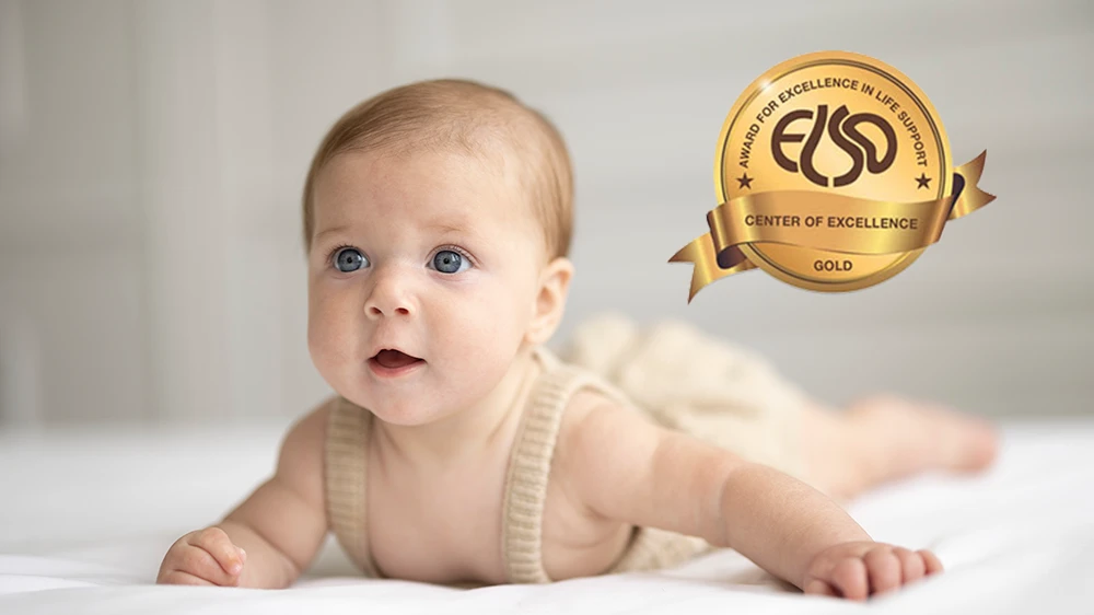 Blue eyed baby laying on tummy raising his head.