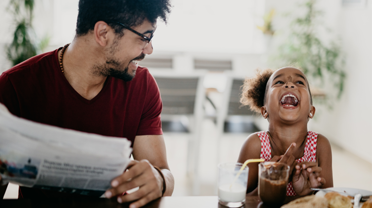 father and daughter laughing as they eat on the kitchen counter.