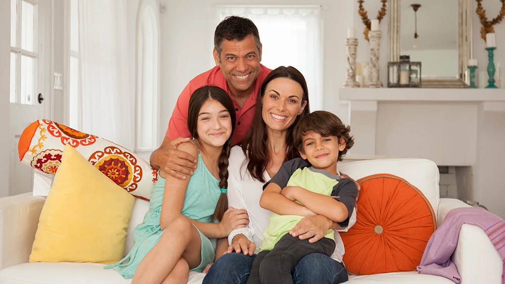 Brunette family of father, mother, teenage girl and boy sitting on couch.