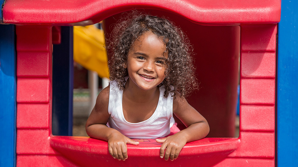 curly haired girl happily leaning out of playhouse.