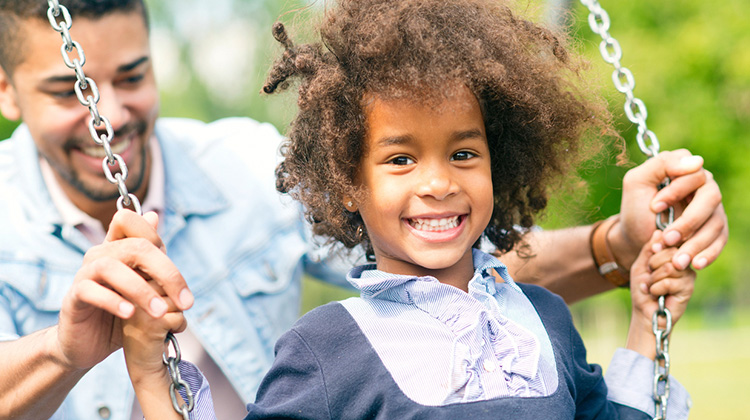 happy african american girl pushed on a swing by her father.